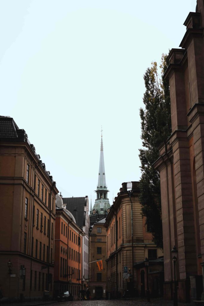 Gångväg i Gamla Stan, Stockholm, som leder till en kyrka. Mörk, mody atmosfär med folktomma kullerstensgator och gammaldags lyktor som lyser svagt.