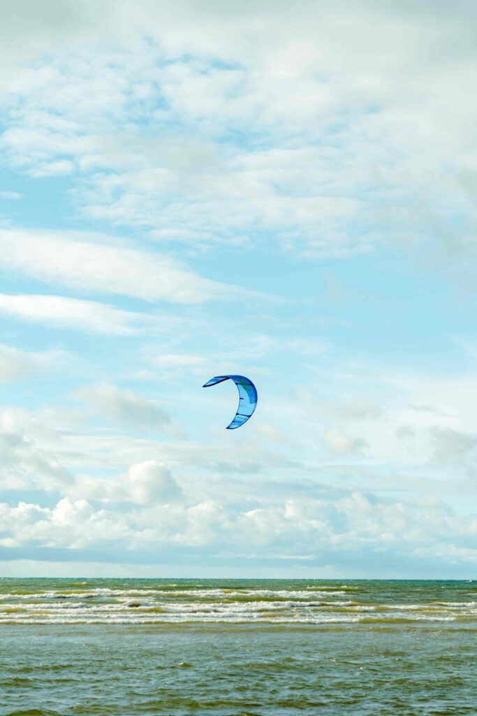 Kitesurfare i Apelviken på blåsig höstdag, omgiven av vågiga blå vatten och delvis klar himmel med spridda vita moln.