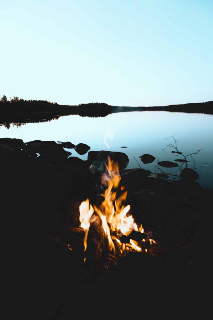 Lägereld vid en stilla sjö i skymningen med spegelblank vattenyta