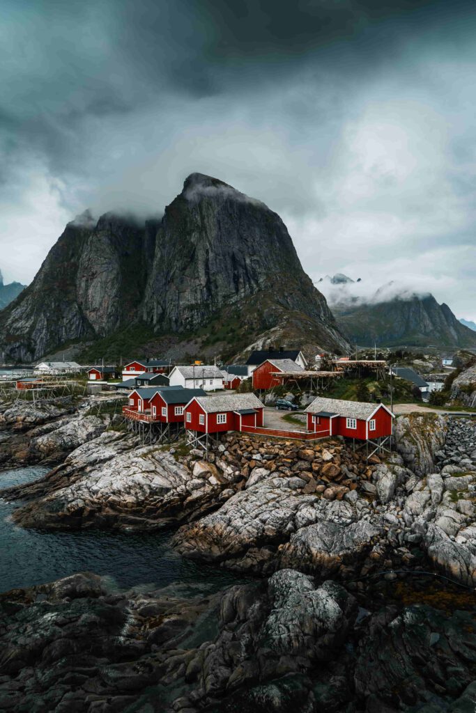 Ett vykort från en norsk fiskeby med röda stugor vid foten av höga berg.