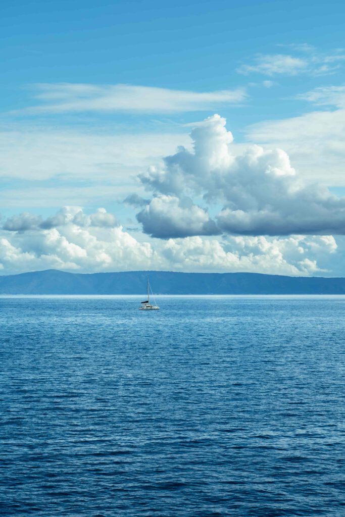 en vit segelbåt seglar på ett lugnt hav under en klarblå himmel med vita moln.