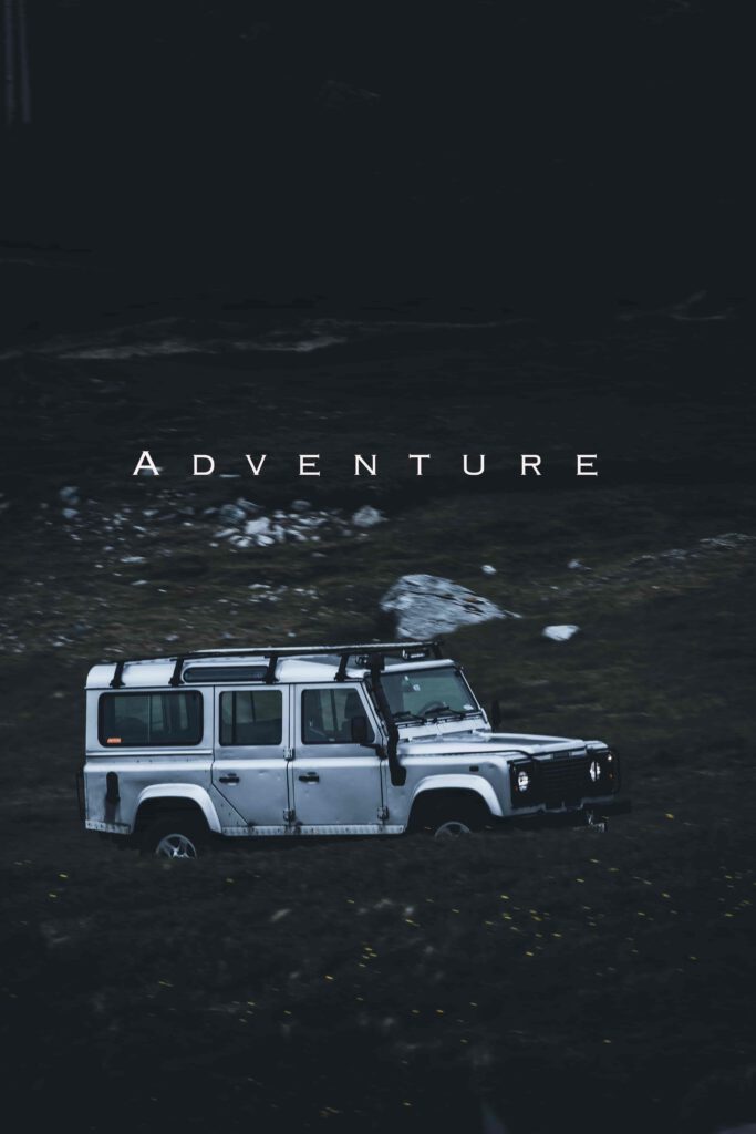 En silvergrå Land Rover Defender kör genom ett mörkt landskap med ordet "ADVENTURE" skrivet ovanför.