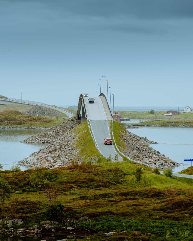 En bågformad bro över ett smalt sund i Norge, med bilar som kör över bron.