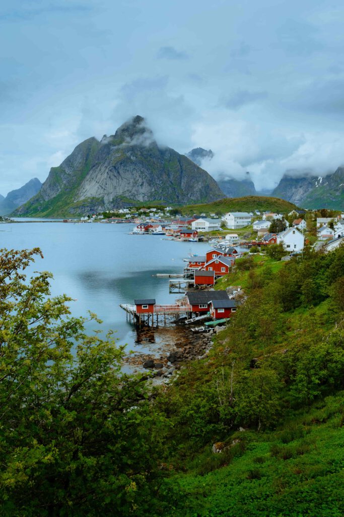 En vy över en norsk kustby med röda fiskebodar och berg i bakgrunden.