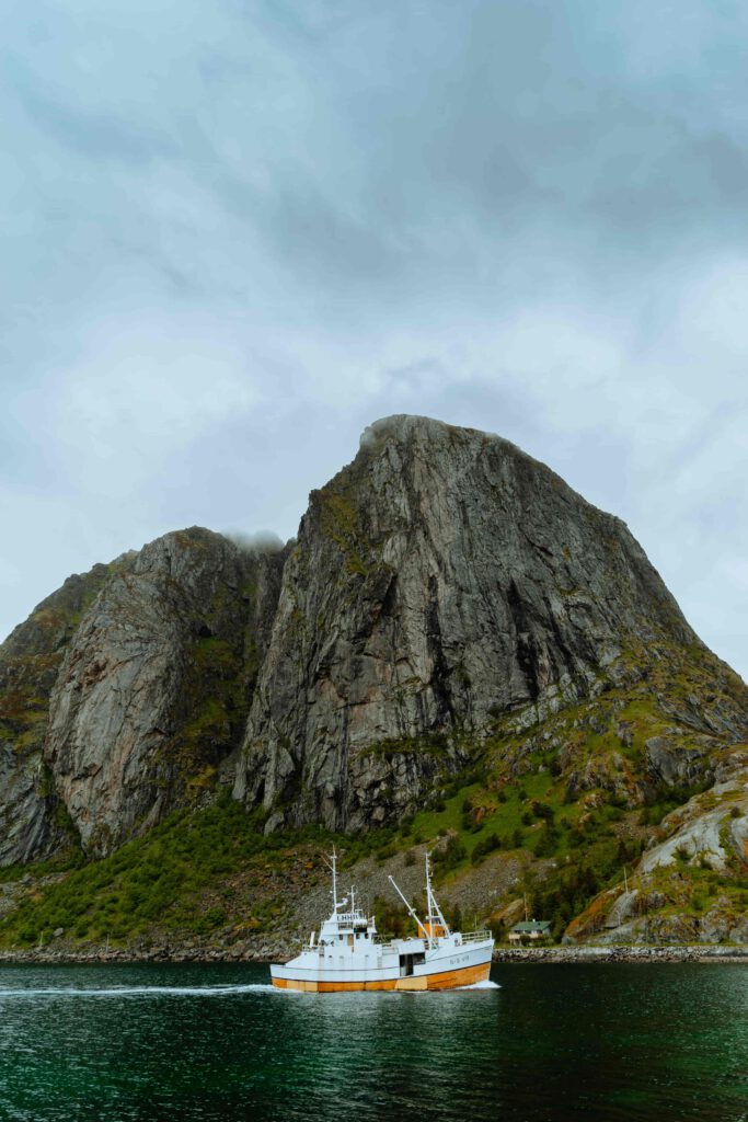 Ett fiskefartyg seglar mot ett stort, mörkt berg i Norge.